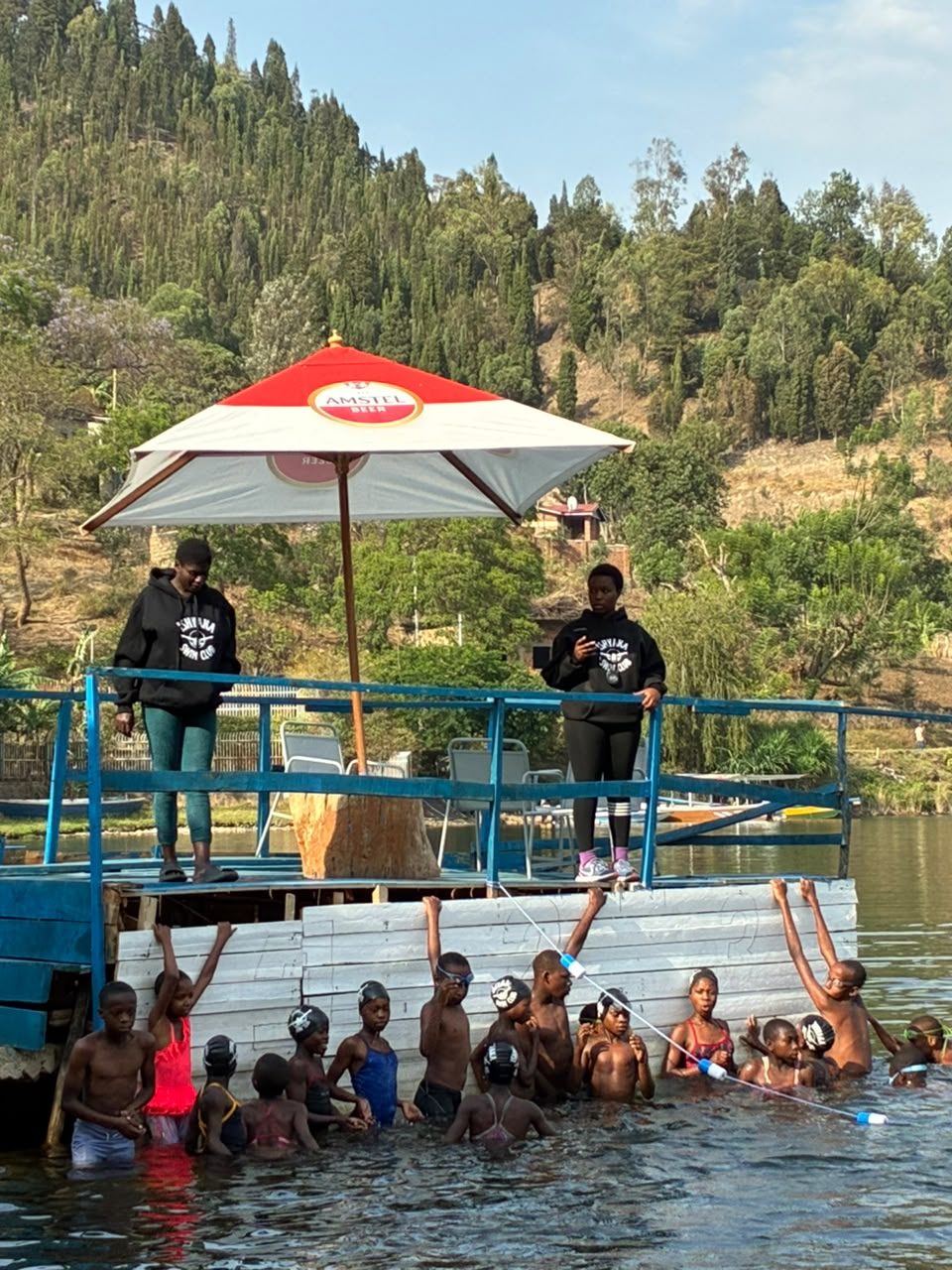 Rwandan coaches on deck beside swimmers in Lake Kivu